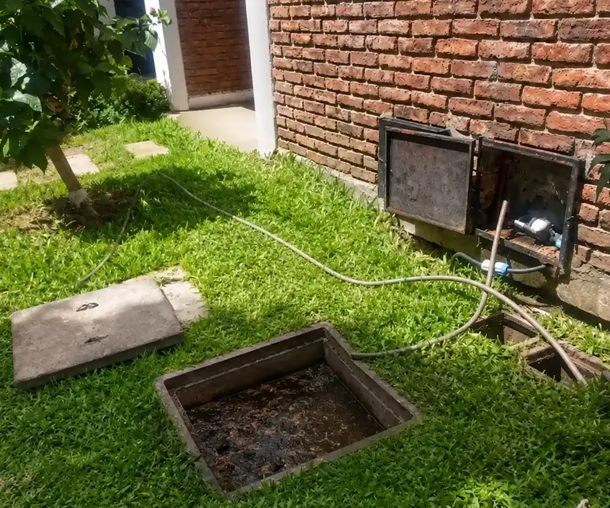 Cámara exterior abierta con agua oscura y una tapa apoyada en el césped
